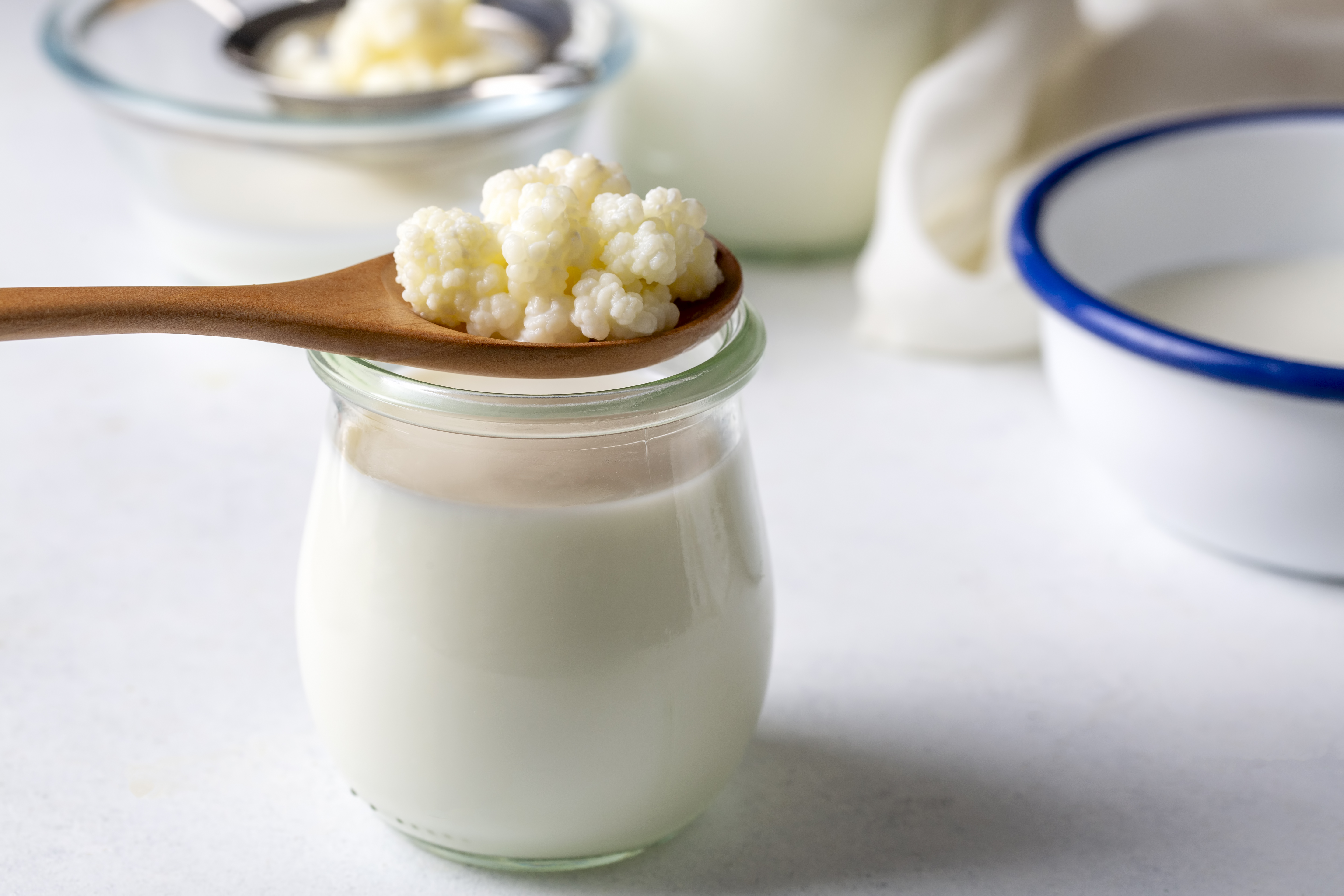 Kefir grains on a spoon over a jar of yogurt
